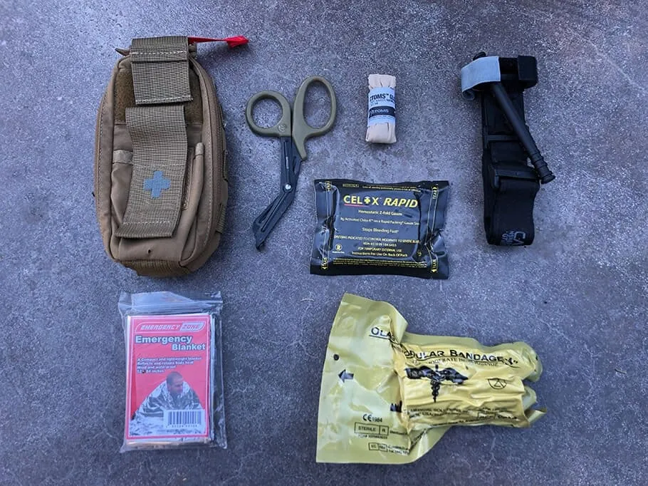 Individual First Aid Kit (IFAK) contents showing tactical pouch, CAT tourniquet, Celox Rapid hemostatic gauze, trauma shears, Israeli pressure bandage, and emergency blanket for trauma response